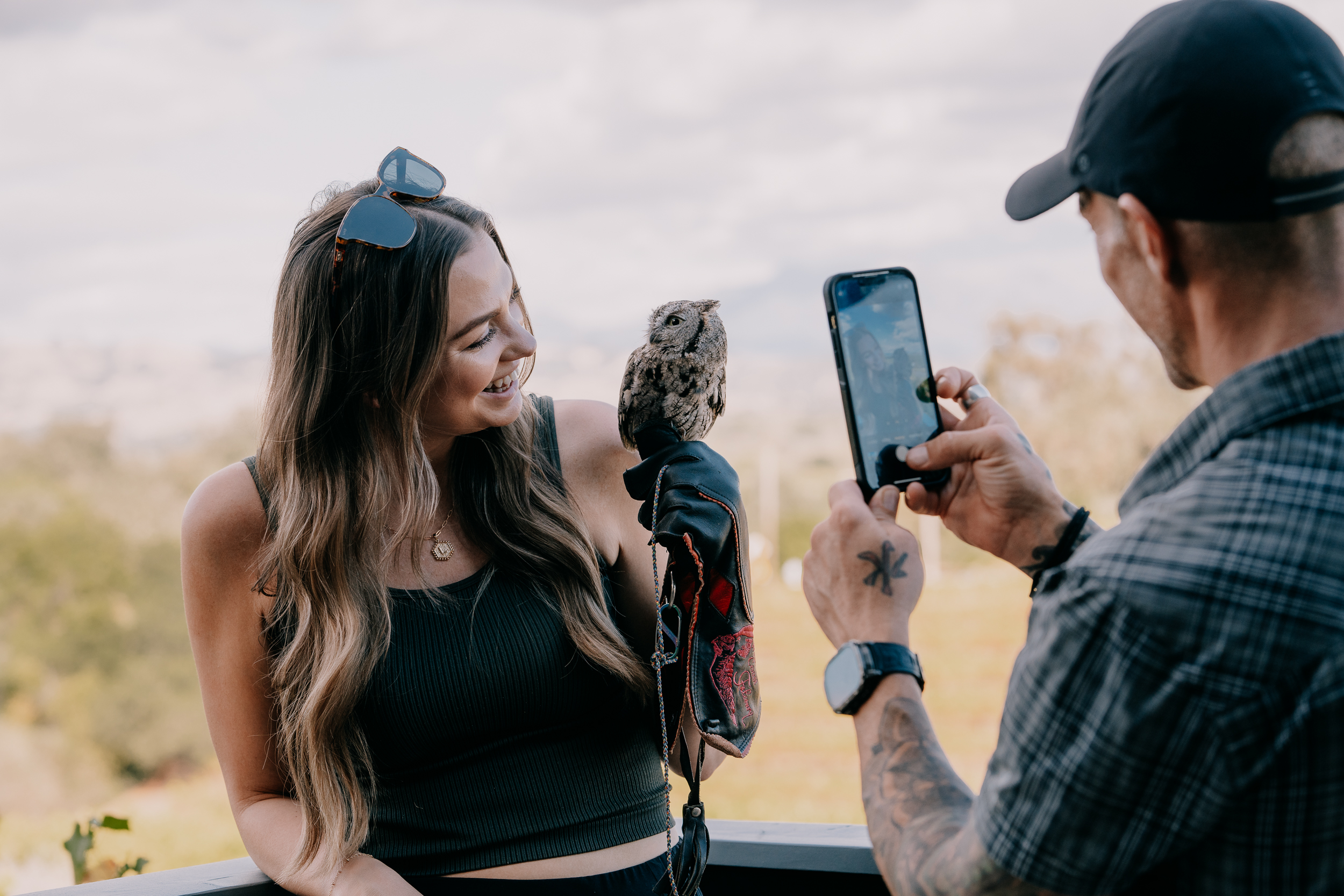 Woman holding an owl while someone takes her picture with a smartphone