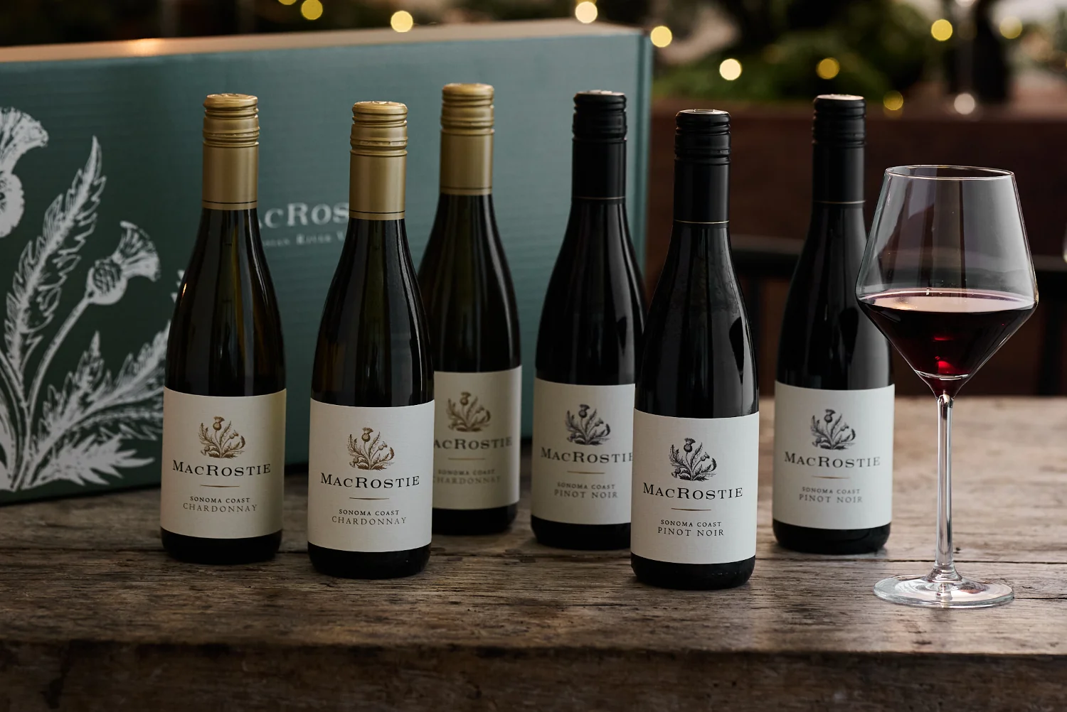 Bottles of MacRostie wine on a table next to a gift box and glass of wine.