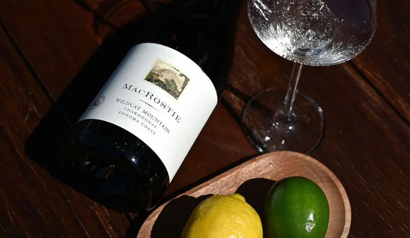 Bottle of Wildcat Mountain Chardonnay next to a glass of wine, a lemon, and a lime