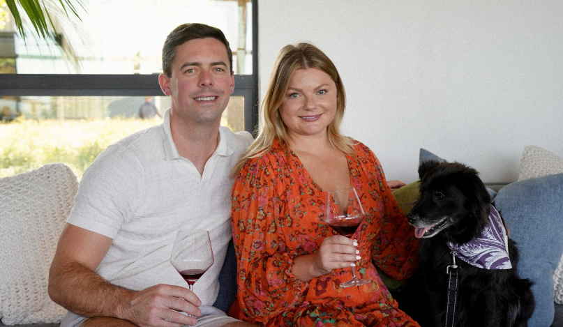 A couple with their dog sitting on a couch at the MacRostie Estate House raising wine glasses