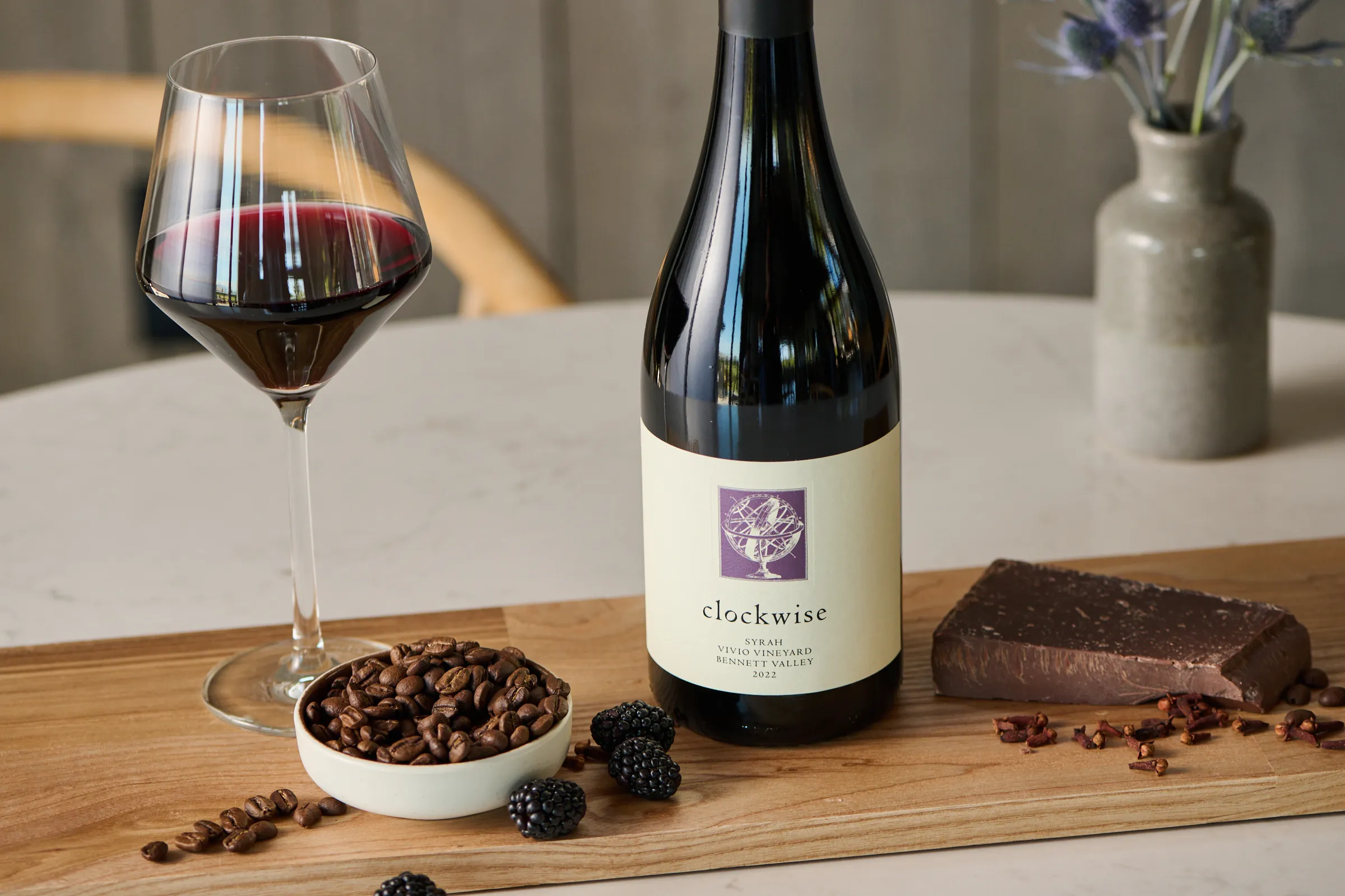 Bottle of Clockwise Syrah next to food pairings and a glass of wine.
