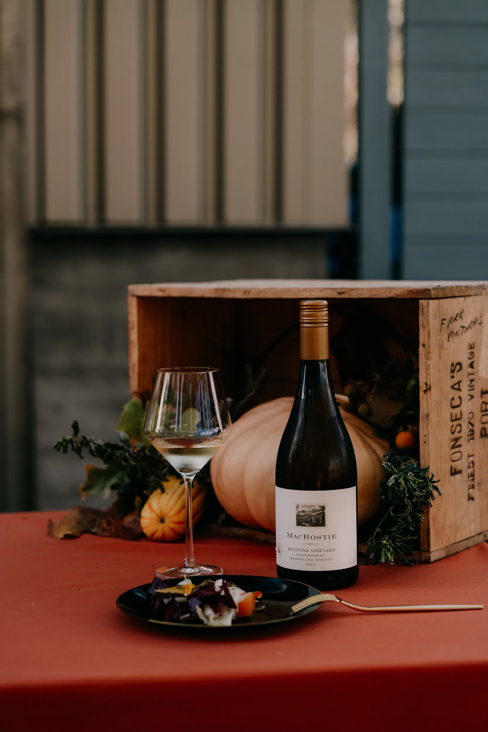 Bottle of Milovina Chardonnay on a table next to a box and squashes