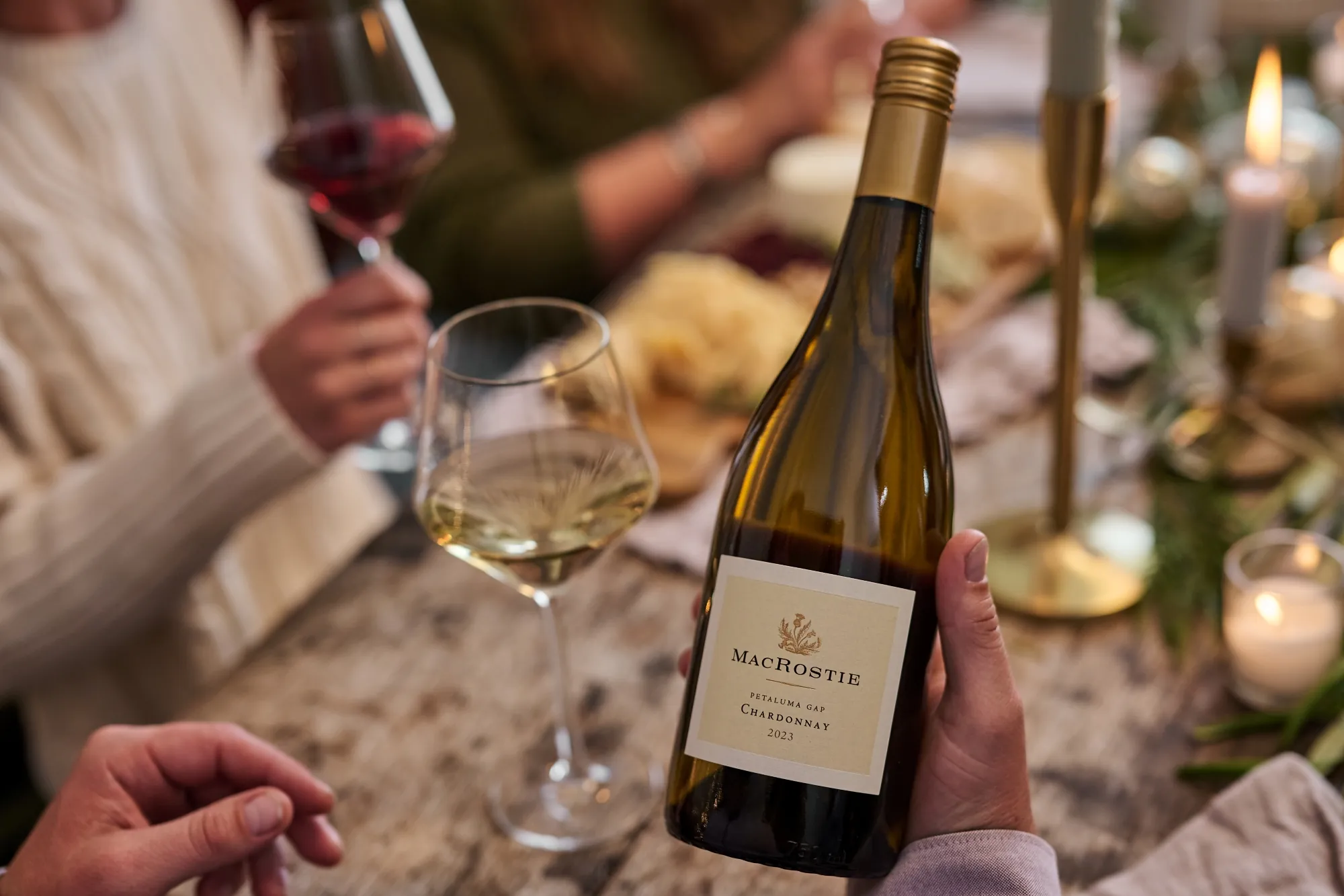 Hands holding a bottle of MacRostie wine and a dinner table with holiday decor in the background