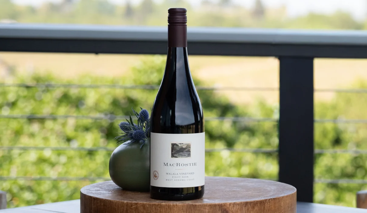 Bottle of Walala Vineyard Pinot Noir next to a vase with purple thistles