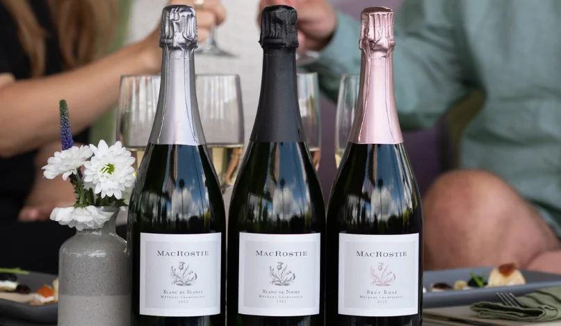 Bottles of MacRostie sparkling wines with people cheersing in the background