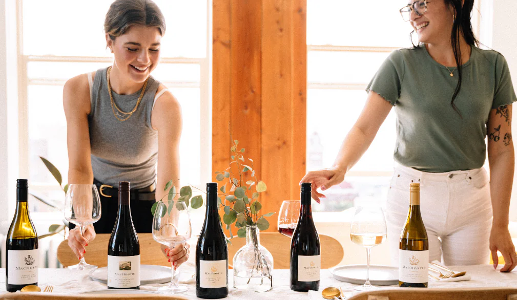 Two people setting a table arranged with MacRostie wine bottles
