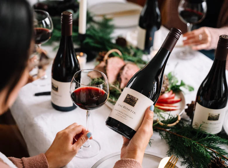Person looking at wine bottle while holding glass over a holiday set table